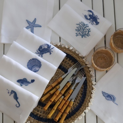 Guardanapos brancos bordados com motivos marinhos azuis e facas com cabos de madeira em mesa branca
