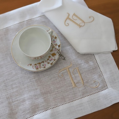 Conjunto de chávena e pires decorados com flores e dourado, guardanapo e pano de linho branco com monogramas bordados.