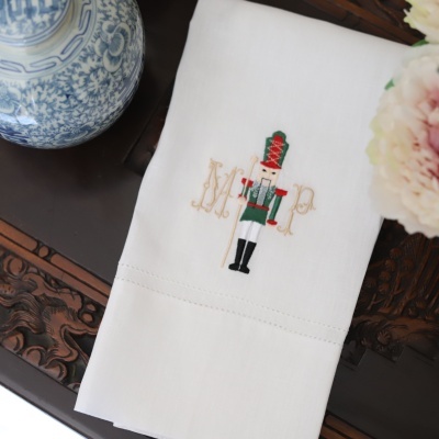 Guardanapo branco com bordado de soldado e letras MP, sobre mesa de madeira escura entalhada