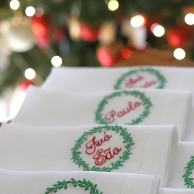 Guardanapos brancos com bordados verdes e nomes vermelhos em fundo difuso festivo