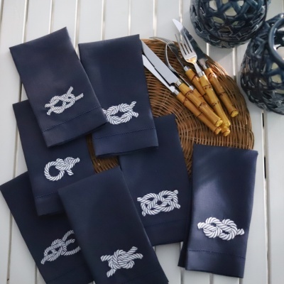 Guardanapos azuis com bordado de nós náuticos, talheres com cabos castanho e objetos decorativos azuis