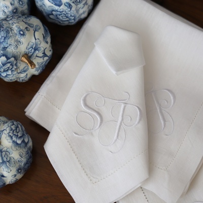 Guardanapos de tecido branco com monograma e maçãs decorativas em porcelana azul e branca
