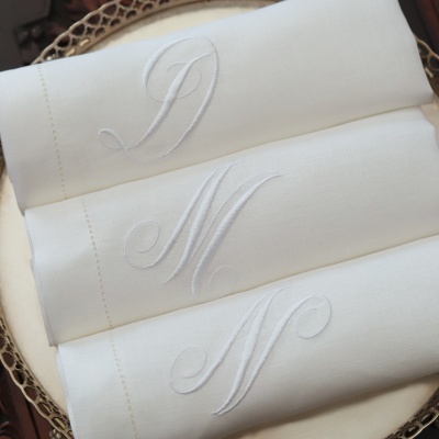 Toalhetes de linho branco com iniciais bordadas D, M e N sobre bandeja prateada