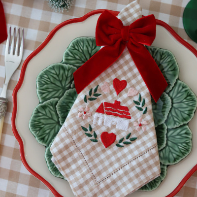 Guardanapo xadrez com bordados e laço vermelho sobre pratos de cerâmica com decoração de folhas e borda vermelha