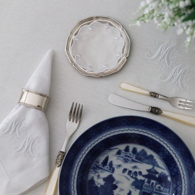 Conjunto de louça e talheres sofisticado com guardanapo monogramado e prato azul. 