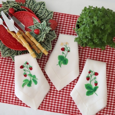 Facas com cabos em bambu sobre prato cerâmico decorativo com guardanapos bordados e toalha xadrez vermelha e branca com planta verde.
