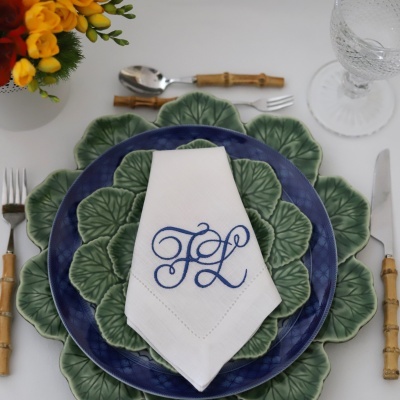 Conjunto de pratos verdes e azuis com guardanapo branco monogramado, talheres e copo num prato decorativo