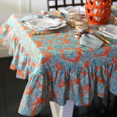 Toalha de mesa floral azul e laranja com pratos brancos e copos com suporte de corda