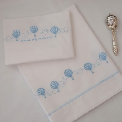 Conjunto roupa bebé branca com bordado azul de balões e frase, com chocalho prateado ao lado