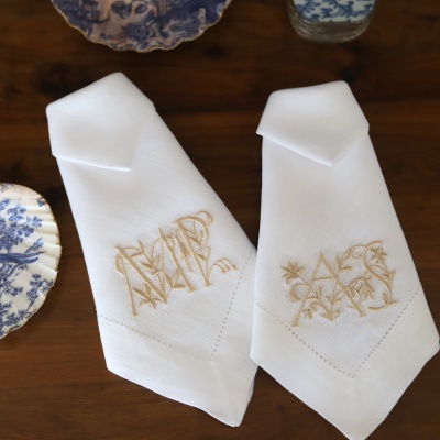 dois guardanapos brancos bordados com letras douradas sobre mesa de madeira