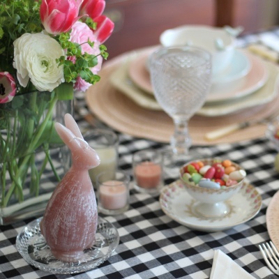 Mesa posta com toalha xadrez, pratos, copo texturizado, flores e estátua de coelho