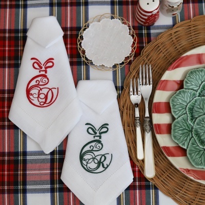 Guardanapos brancos bordados com monogramas parecidos a peras sobre toalha riscada e prato decorativo