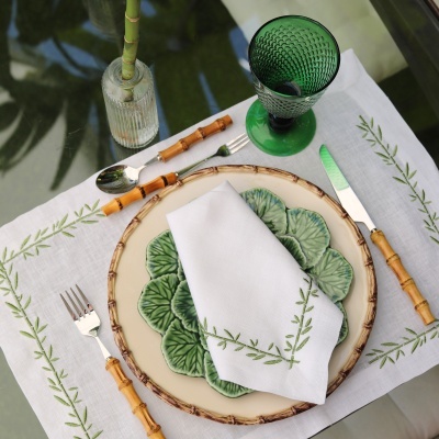 Mesa posta com pratos creme e verde, talheres com cabo de bambu, guardanapo branco bordado e copo verde.
