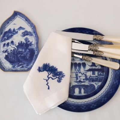 Prato e travessa de porcelana azul e branca, guardanapo branco bordado e três facas com cabo creme