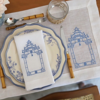 Mesa posta com louça azul e branca, guardanapo e toalha bordados, talheres com cabo de bambu e copo com capa de corda.