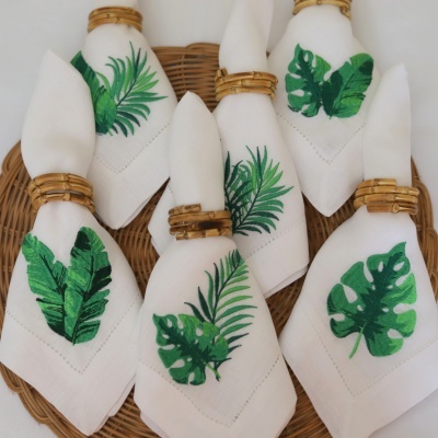 Seis guardanapos brancos com folhas verdes e argolas de madeira num cesto de vime