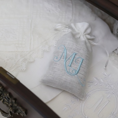 Saco bordado com as letras MJ sobre tecidos brancos bordados em caixa de madeira