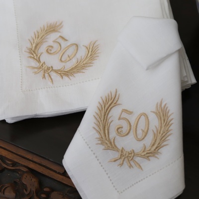 Guardanapos brancos com bordado dourado do número 50 em forma de coroa de folhas.