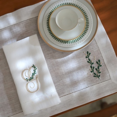 Conjunto de loiça com chávena e prato em porcelana branca com padrão verde e dourado sobre toalha bordada
