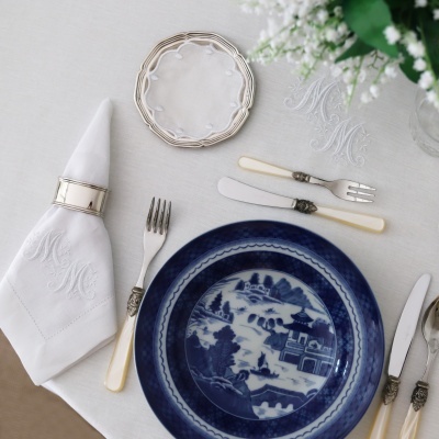 Conjunto de louça azul e branco com talheres e guardanapo monogramado em mesa branca