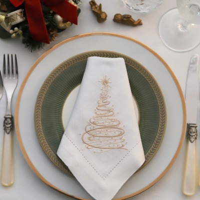 Conjunto de pratos verde e branco com guardanapo bordado, talheres e copos numa mesa decorada para Natal