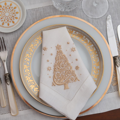 Conjunto de loiça com pratos branccos e padrão dourado floral, guardanapo branco bordado, copos de vidro e talheres com cabos creme.