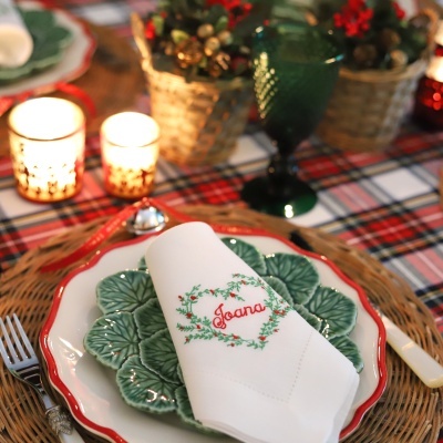 Mesa posta com prato branco e verde, guardanapo bordado com o nome Joana, copo verde e decoração natalina