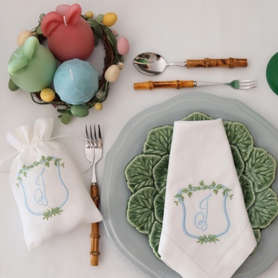 Mesa posta com velas de coelho, guardanapo bordado, pratos em forma de folha e talheres com cabos de madeira.