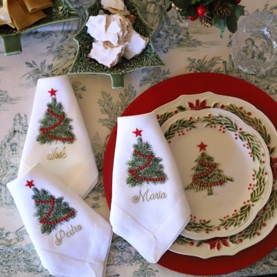 Guardanapos de Natal bordados com nomes e pratos decorativos em mesa festiva