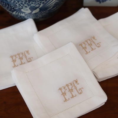 Guardanapos brancos com monograma dourado FFC e cerâmica azul e branca ao fundo