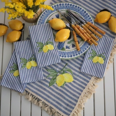 Guardanapos e toalha azul e branca com limões, pratos azuis e talheres de madeira sobre mesa branca