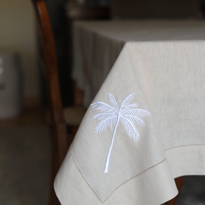 Toalha de mesa bege com bordado branco de uma palmeira no canto