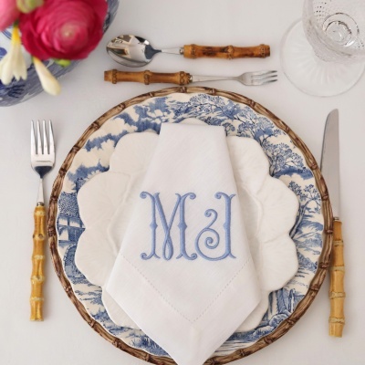 Mesa posta com prato azul e branco, guardanapo branco monogramado, talheres com cabo de bambu e copo de vidro.