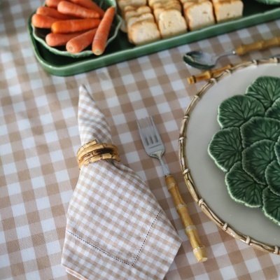 Mesa posta com guardanapo xadrez bege, talheres com cabo de bambu e prato branco com decoração verde.