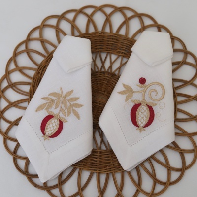 Dois guardanapos brancos com bordado de romã e folhas sobre tapete de palha circular