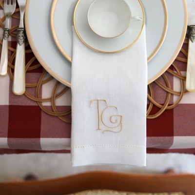 Conjunto de louça branca com detalhes dourados e guardanapo branco com monograma TG
