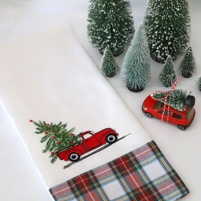 Toalha branca com bordado de carrinha vermelha e árvore de Natal, com padrão quadriculado colorido na base