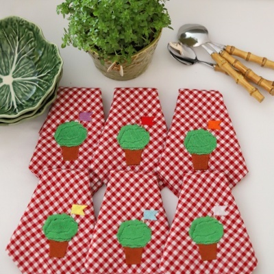 Panos de cozinha xadrez com bordado, pratos de cerâmica verde, plantinha em vaso e colheres com cabo de madeira.