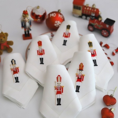 Conjunto de guardanapos brancos com bordados de soldados em uniforme vermelho e preto, decoração natalícia ao fundo