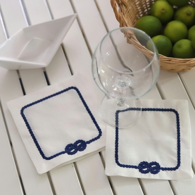 Guardanapos brancos bordados, copo de pé transparente, cesta de vime com maçãs verdes numa mesa branca