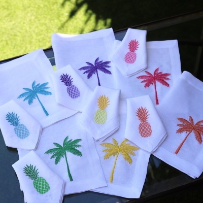 Toalhas brancas bordadas com palmeiras e ananases coloridos em várias cores sobre superfície preta