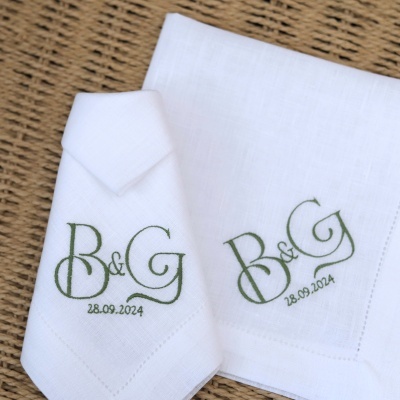 Panos de tecido branco com bordado verde mostrando as iniciais B & G e a data 28.09.2024