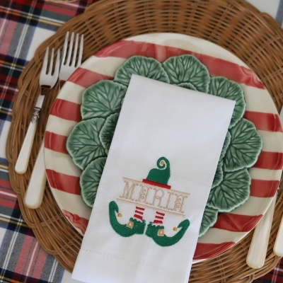 Mesa posta com prato decorativo, guardanapo branco bordado e talheres sobre toalha xadrez.