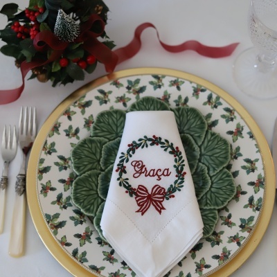 Jogo de jantar com prato de porcelana, prato verde em forma de folhas e guardanapo branco bordado com a palavra Graça