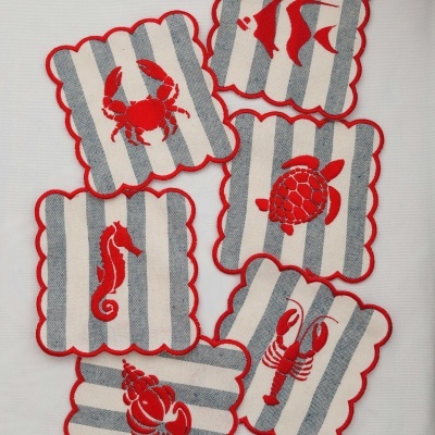 Bases para copos em tecido com listras cinza e branco e bordadura vermelha, com bordados vermelhos de animais marinhos.