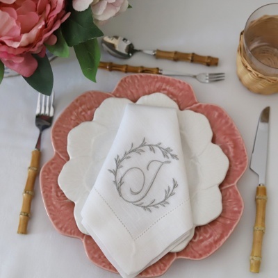 Mesa posta com pratos de cerâmica rosa e branco, talheres com cabo tipo bambu e guardanapo branco bordado com letra J.
