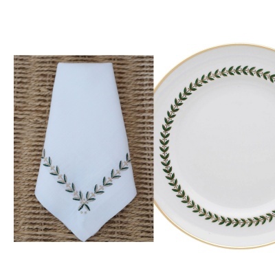 Guardanapo branco bordado e prato branco com padrão de folhas verdes