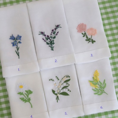Seis panos brancos com bordados florais coloridos numerados, sobre tecido quadriculado verde e branco