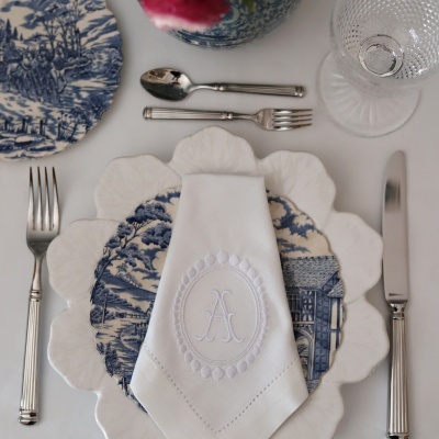 Posto de mesa com pratos brancos e azuis, guardanapo branco com monograma e talheres prateados