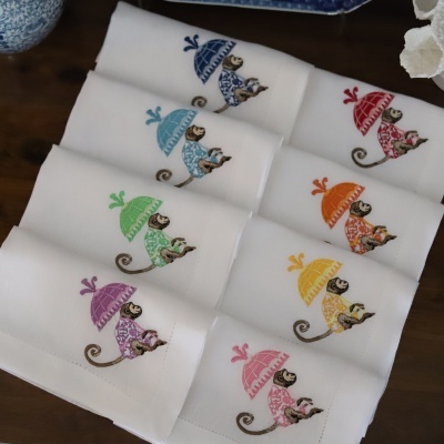 Lenços brancos com bordados coloridos de macacos sob guarda-chuvas em várias cores